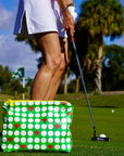 Person on a golf course with a green bag with golf ball pattern, golf club, and ball.