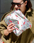 Person holding a silver pouch with cherry design against a gray wall.