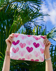 Person holding a pouch with pink heart pattern against a palm tree background