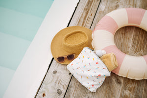 Beach hat, sunglasses and swimmers patterned zipper pouch sitting poolside