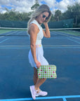 Woman in a white outfit holding a tennis pouch with red hearts on a tennis court.