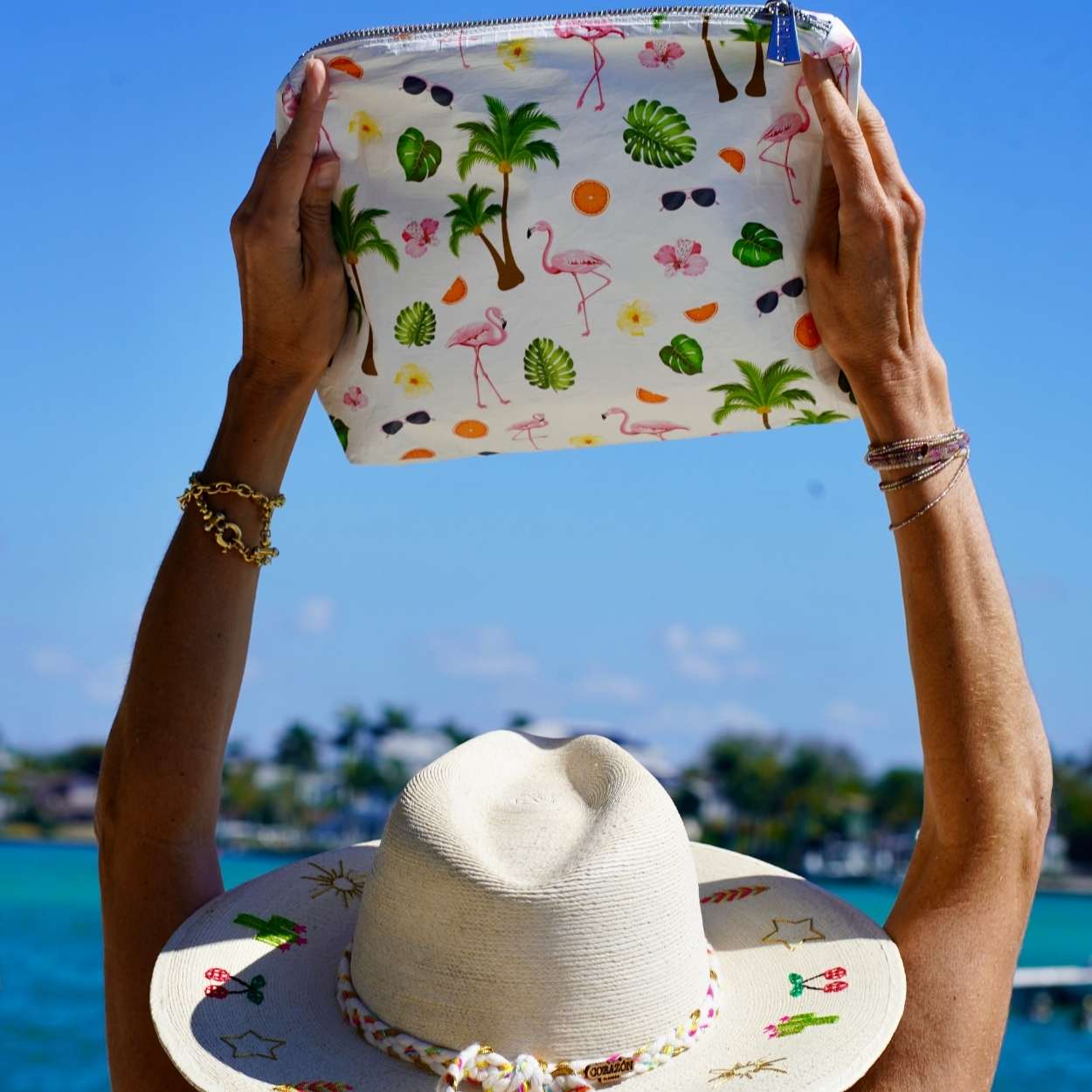 Person holding a colorful pouch with tropical patterns against a clear blue sky.