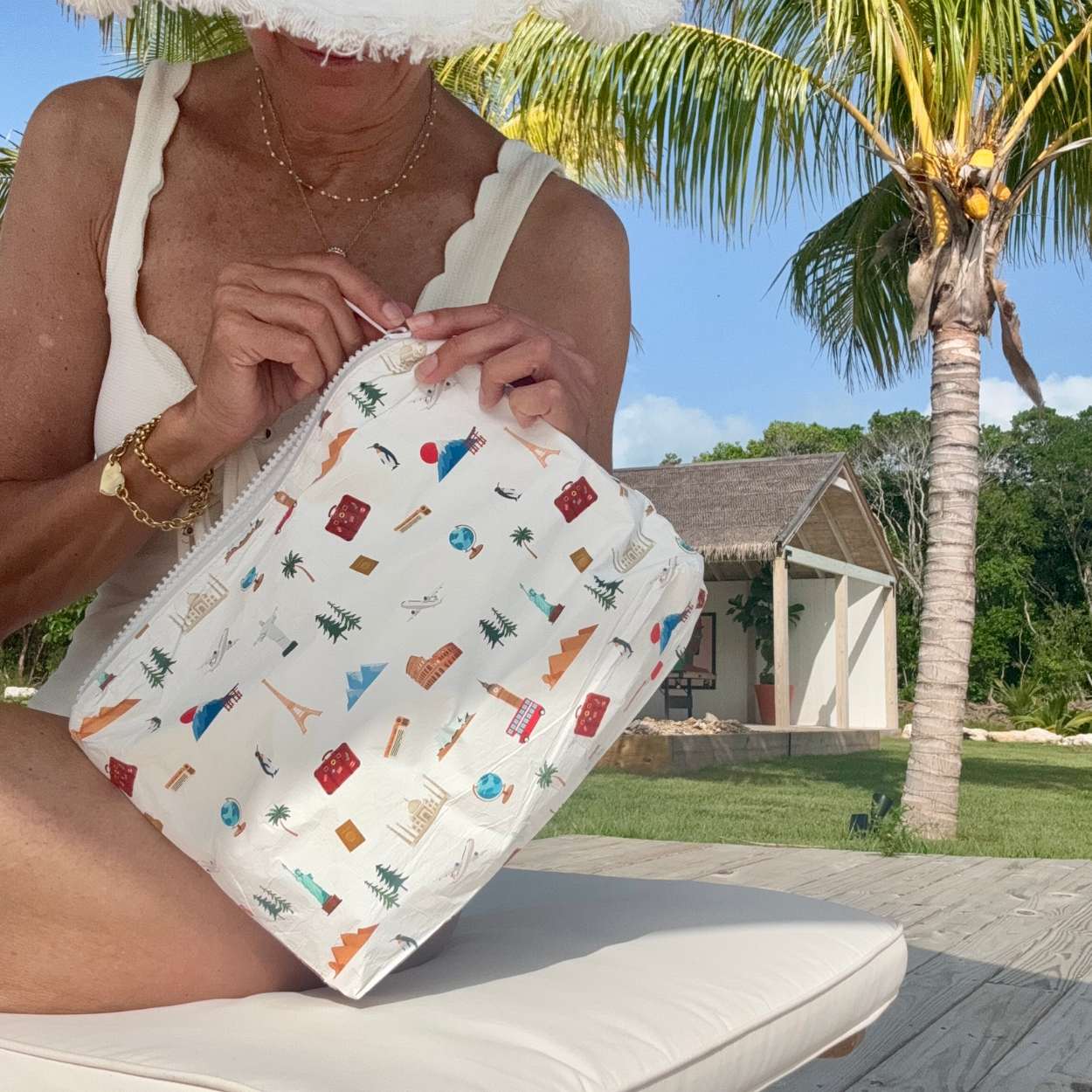 Person holding a landmark patterned pouch outdoors with palm trees and a building in the background