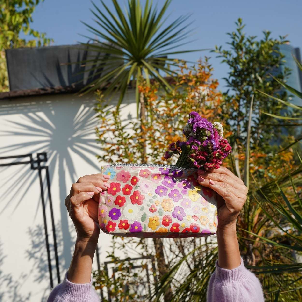 Person holding a floral pouch with flowers against a garden background