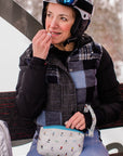 Woman on ski lift holding a white with skier pattern zip wristlet