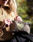 Woman wearing a bronze metallic mini pouch with a gold heart design in outdoor setting.