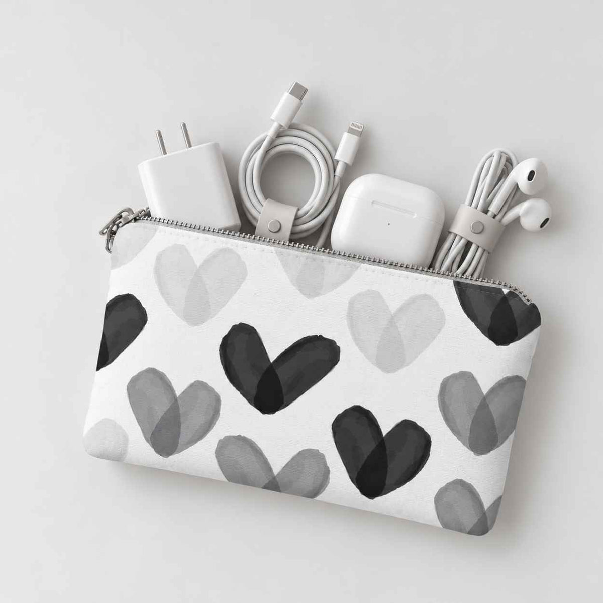 Mini zip pouch with black and white heart print containing various tech items on light gray background. 