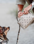 Person holding a bandana patterned pouch with a small dog on a leash