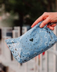 Hand holding a blue bandana patterned pouch with a heart design outdoors.