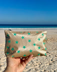 Mini beige zipper pouch with sea green stars in front of ocean