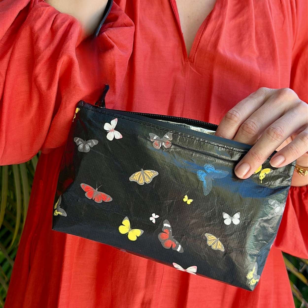 Person holding a black pouch with colorful butterfly patterns against a red garment background