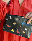 Person holding a black pouch with colorful butterfly patterns against a red garment background