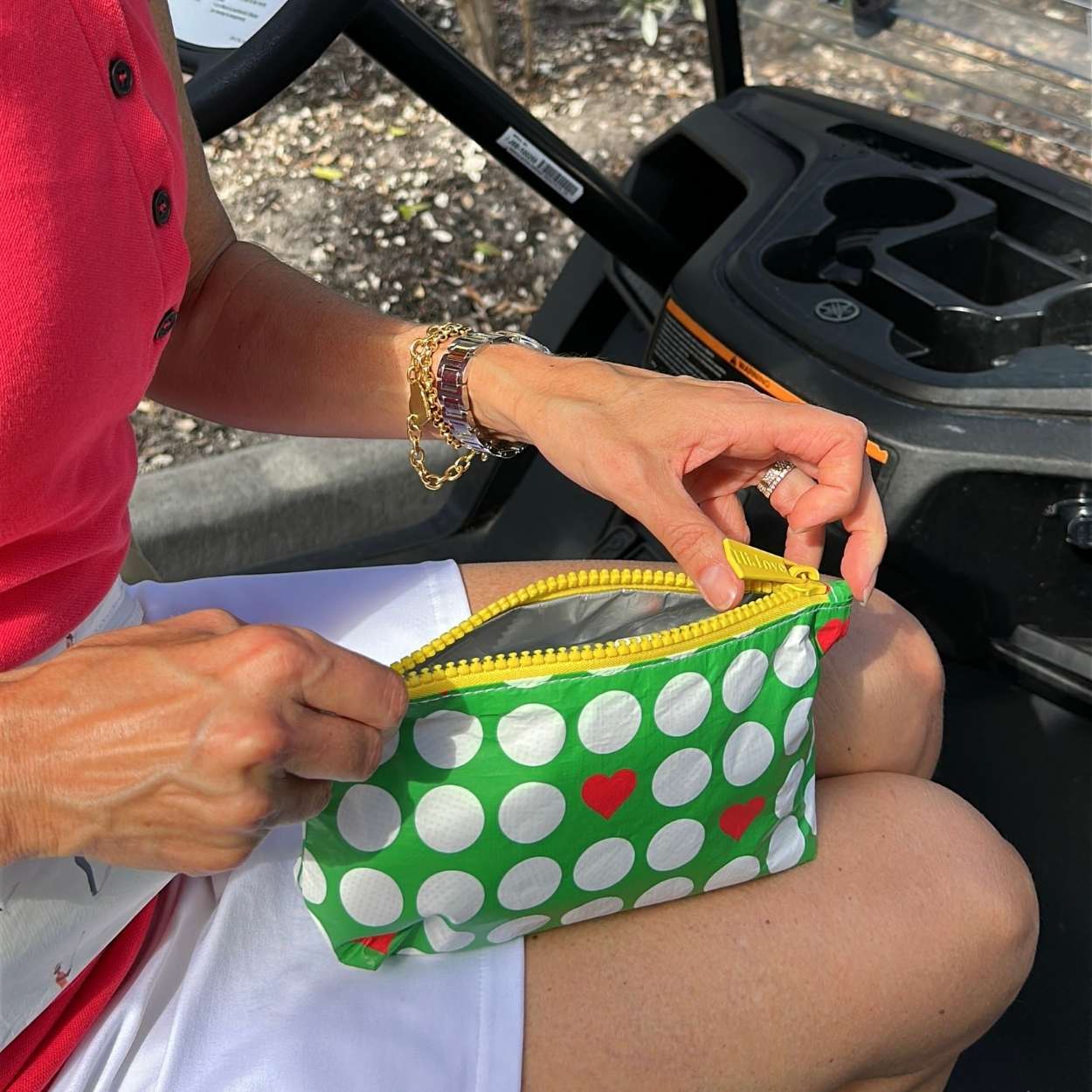 Person holding a green pouch with white golf balls and red hearts on a golf cart seat.