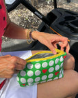 Person holding a green pouch with white golf balls and red hearts on a golf cart seat.