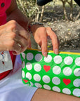 Person holding a green pouch with white golf balls and red hearts outdoors