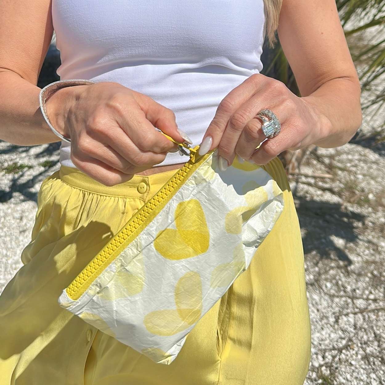 Person holding a yellow pouch with heart designs, wearing a white top and yellow pants.