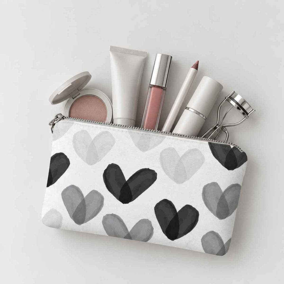 Mini zip pouch in black and white heart print containing various makeup items on light gray background. 