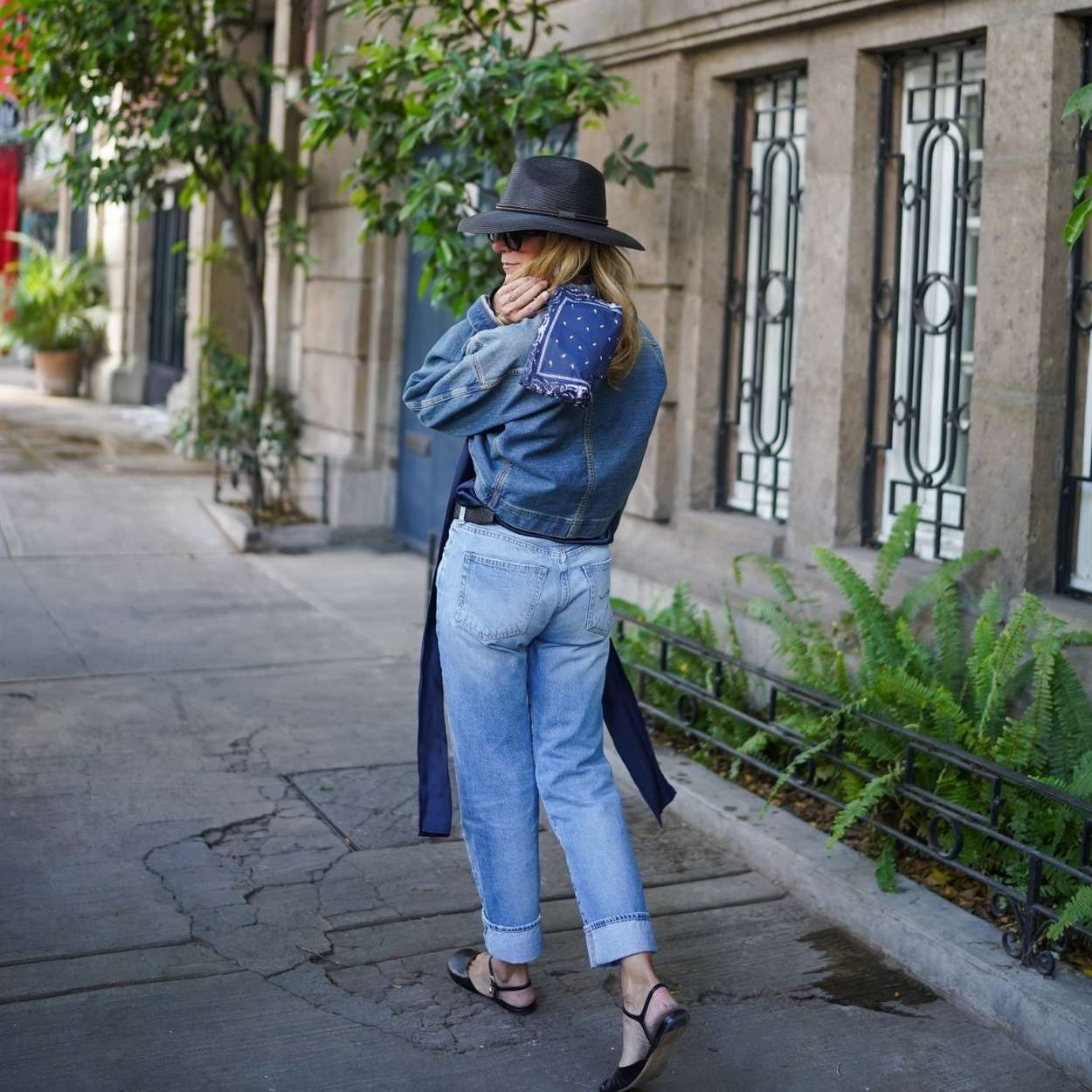 Woman in denim outfit with hat carrying navy bandana pouch walking on a city street