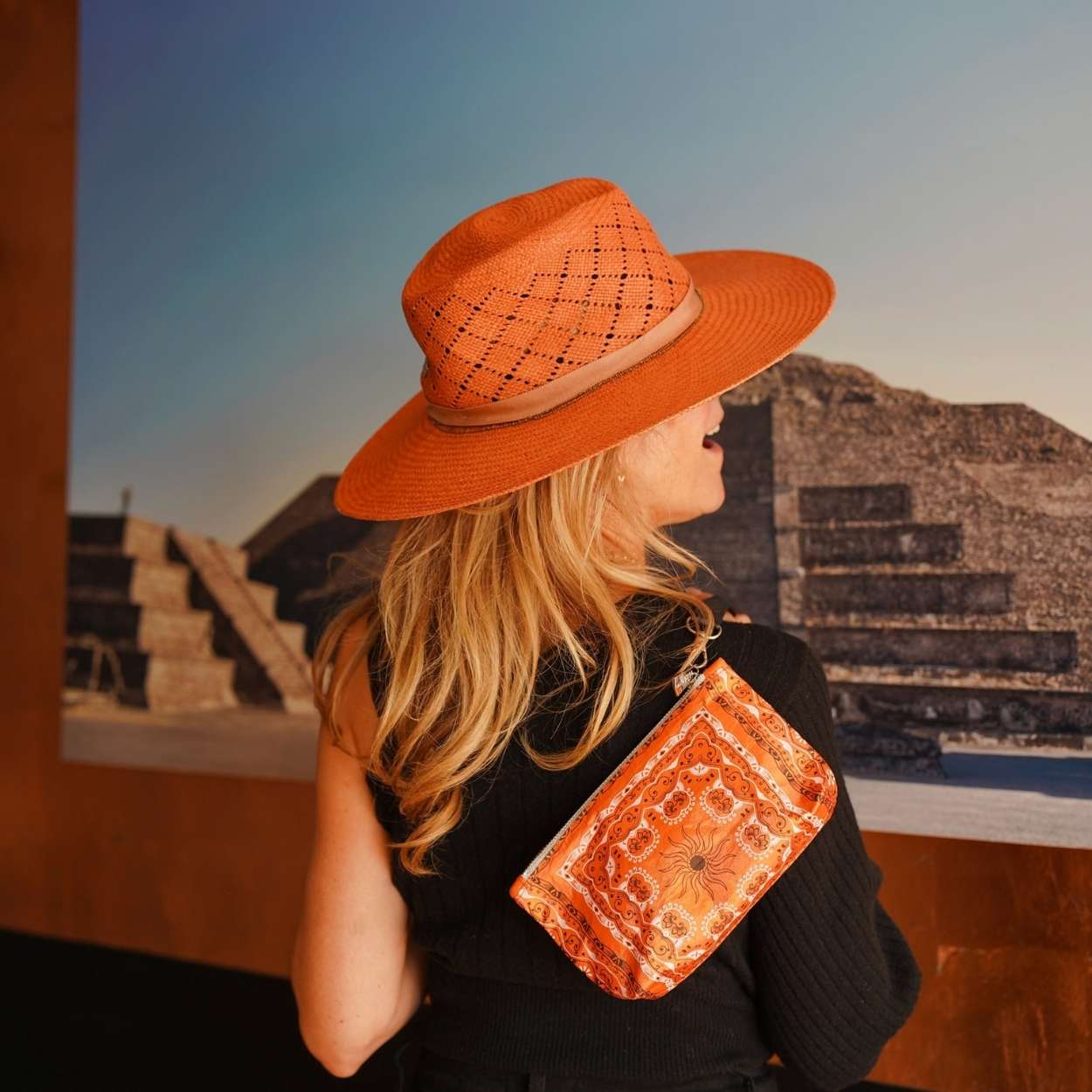 Person wearing an orange hat and matching orange bandana pouch in front of a pyramid-like structure.