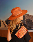 Person wearing an orange hat and matching orange bandana pouch in front of a pyramid-like structure.