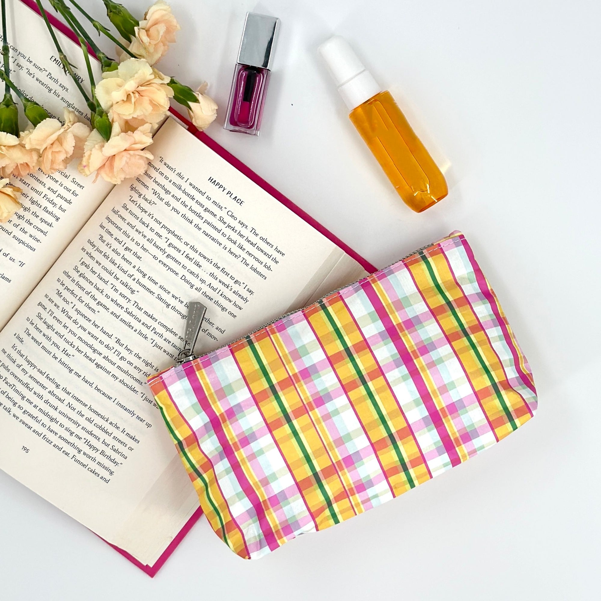 Mini pink and orange plaid zipper pouch laying next to lipstick and perfume 