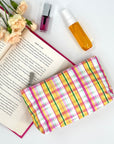 Mini pink and orange plaid zipper pouch laying next to lipstick and perfume 