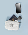 White shimmer mini pouch with silver star holding a phone, sunglasses, and passport, styled as a flat lay on light blue background.