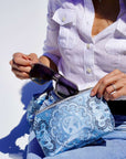 Person holding a blue bandana patterned pouch with sunglasses, wearing a white shirt and jeans.
