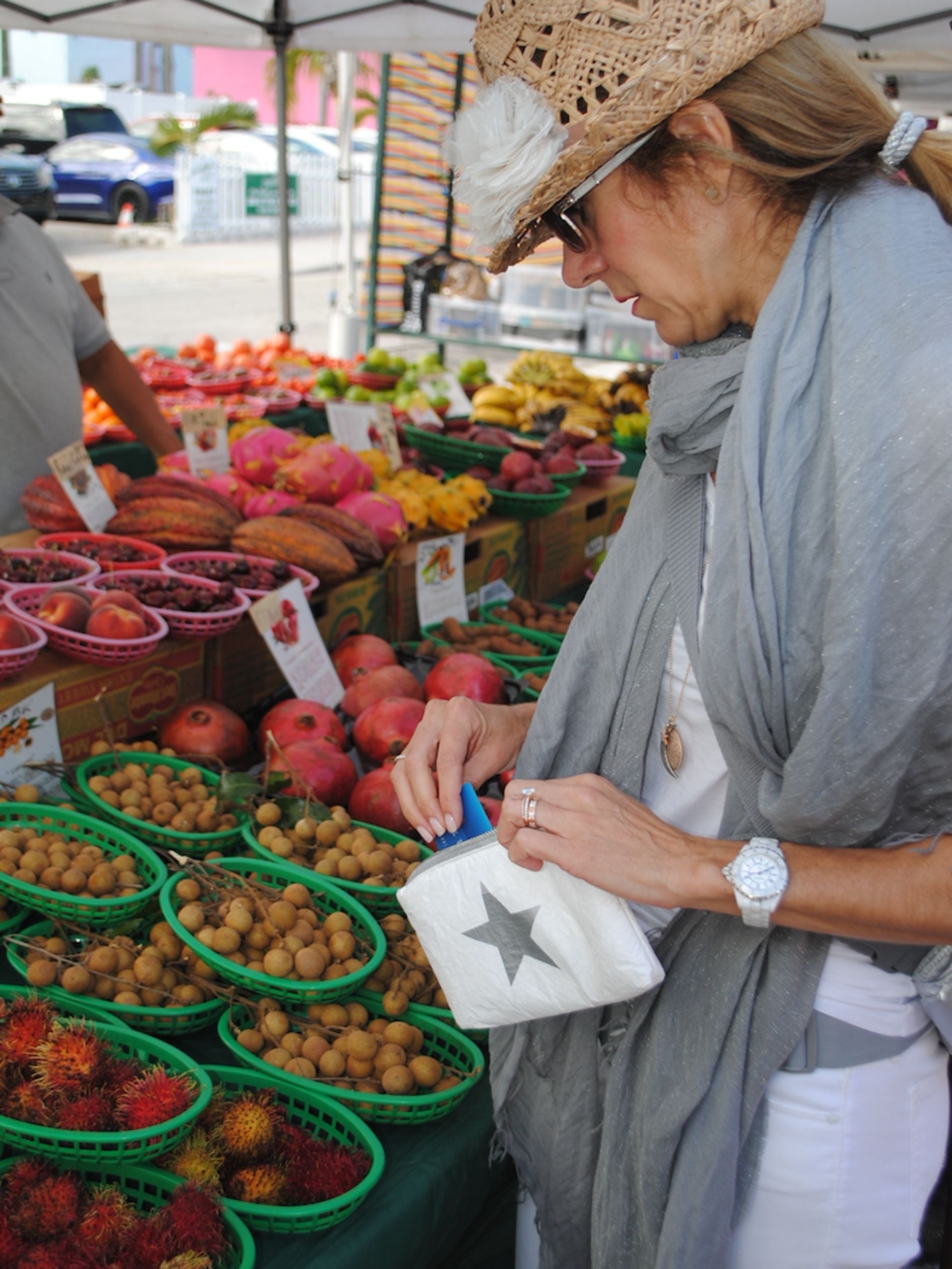 Woman carrying the white shimmer pouch while shopping for produce at an outdoor farmers market.