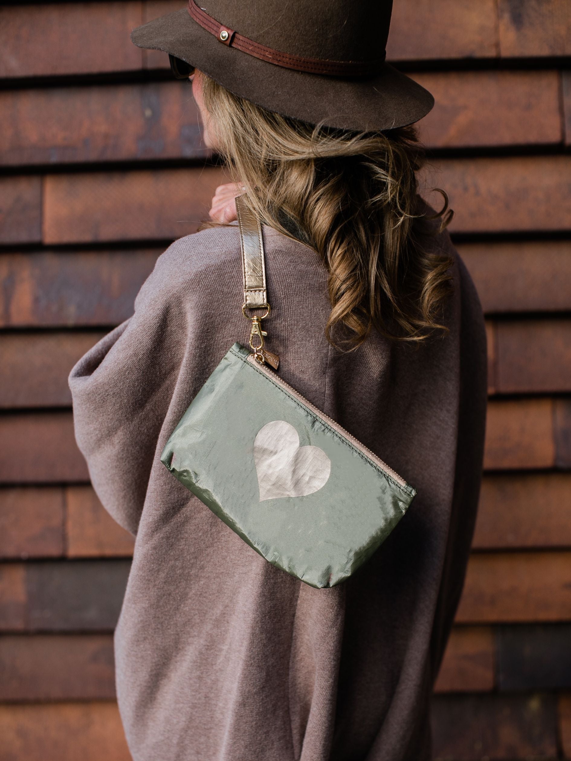 Woman wearing mini green zipper pouch with heart and clip on wristlet strap