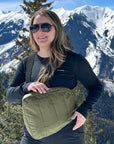 Woman in front of snowcapped mountains wearing a shimmer olive green crossbody backpack