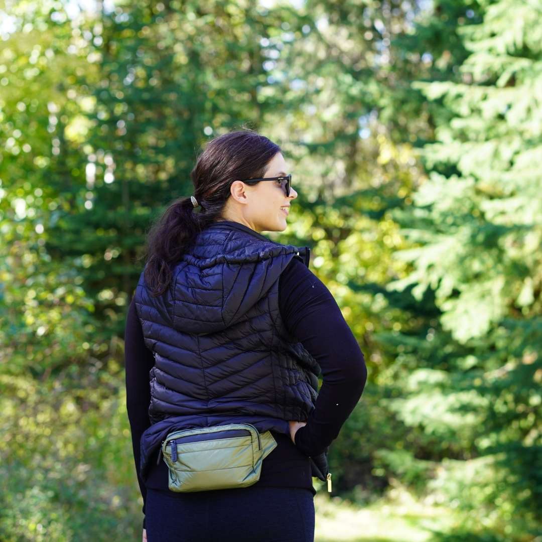 Person wearing a black puffer vest with a green crossbody belt bag in a forest setting