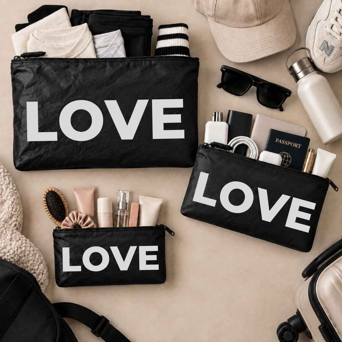 three travel pouches in black with silver LOVE text on beige background with various beauty and travel essentials