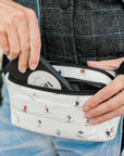Person putting phone in puffer crossbody fanny pack belt bag in dancing skiers pattern