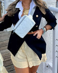 Person wearing a black blazer, white shirt, white fanny pack and beige shorts on a dock.