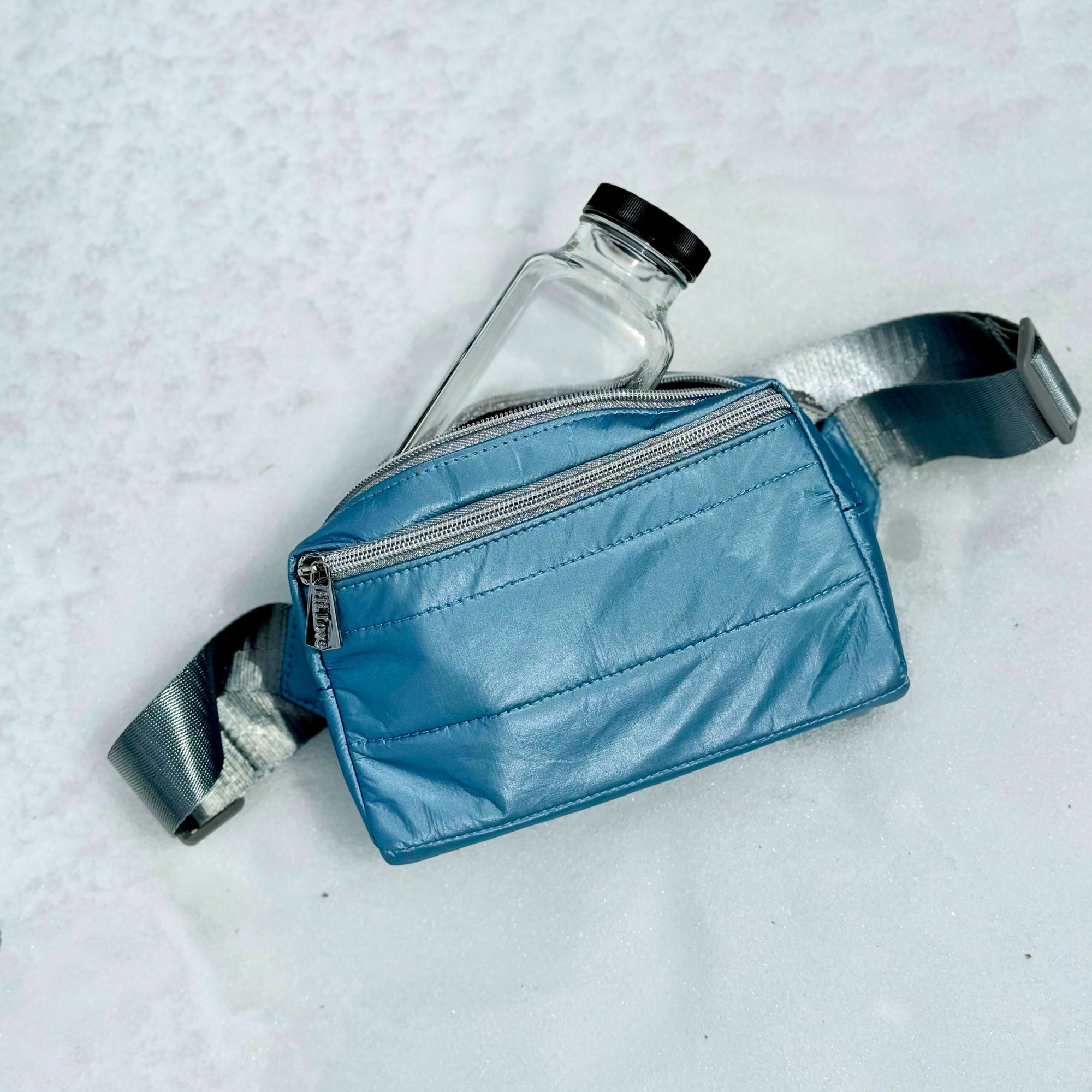 Shimmer ice blue puffer crossbody fanny pack belt bag laying on top of snow