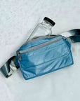 Shimmer ice blue puffer crossbody fanny pack belt bag laying on top of snow
