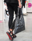 Woman holding a shimmer black top handle puffer tote by her side
