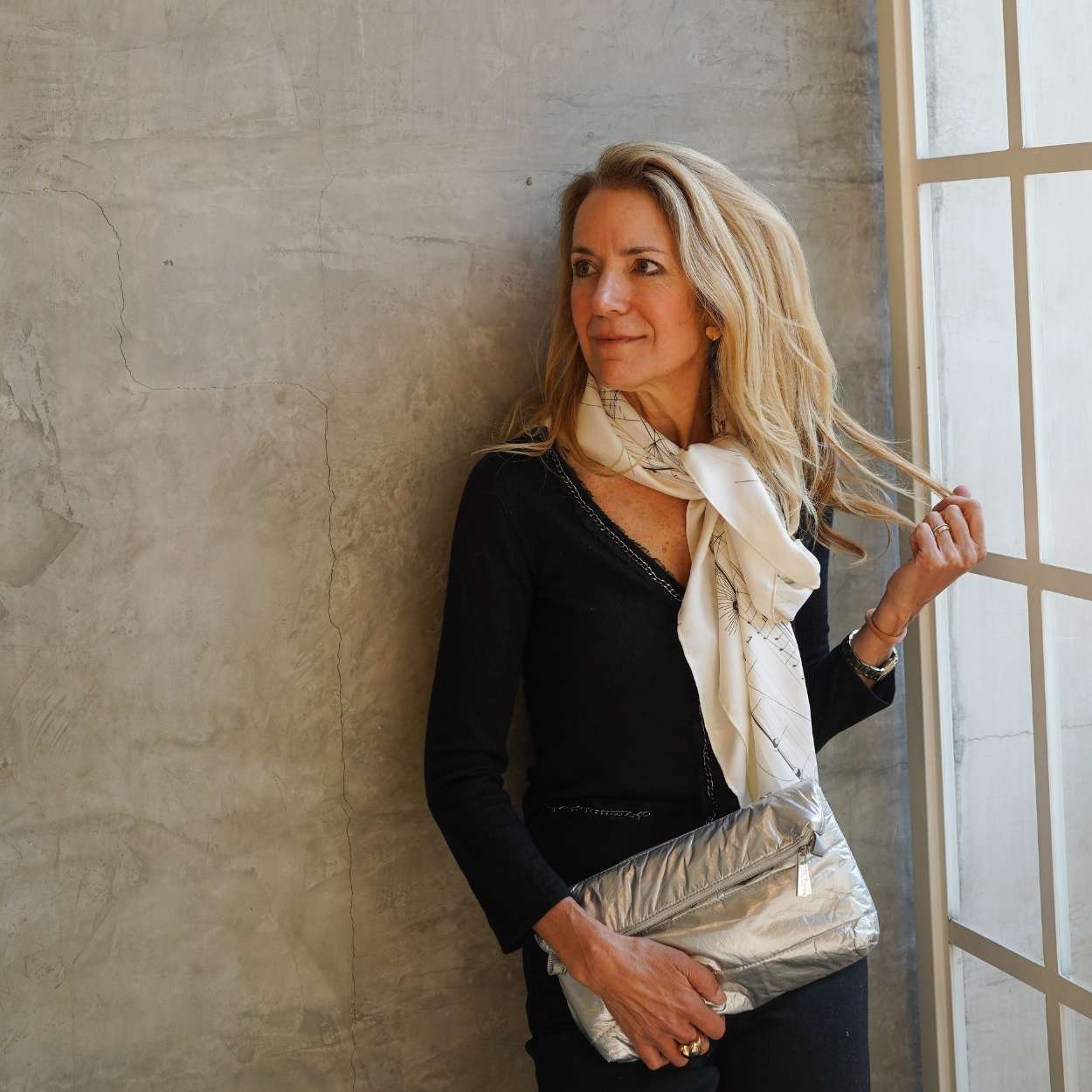 Woman holding a silver clutch against a textured wall
