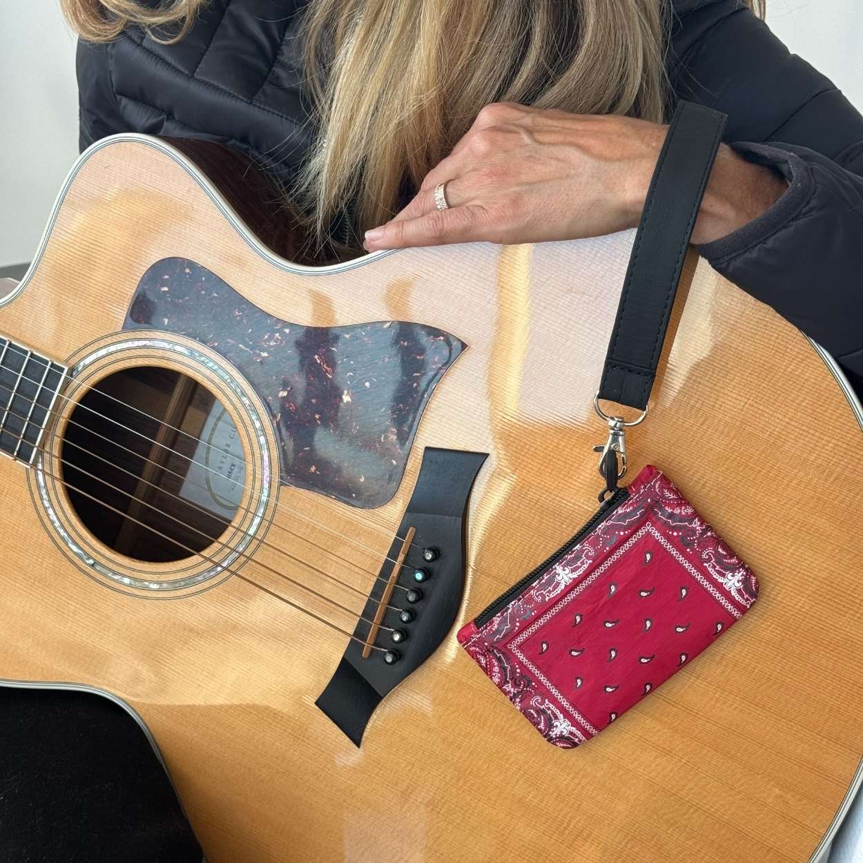 Acoustic guitar with a red bandana pouch attached to the strap