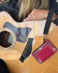 Acoustic guitar with a red bandana pouch attached to the strap