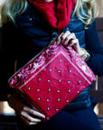 Woman wearing red scarf holding a red bandana patterned zipper clutch bag