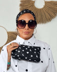 Woman wearing a black silk scarf with hearts, moons and stars as a headband, holding the matching wristlet.