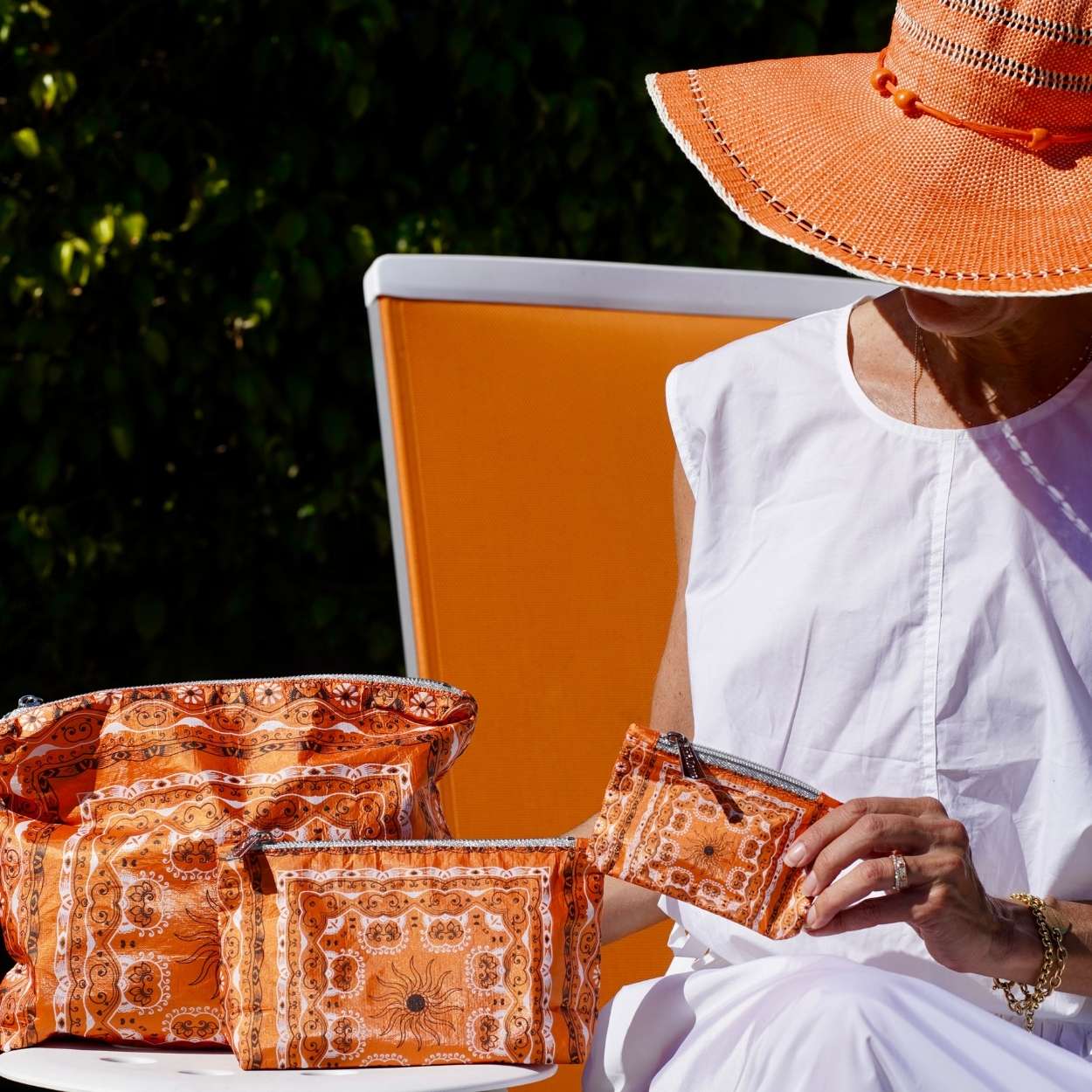 Woman sitting outdoors with orange bandana patterned bags and a hat