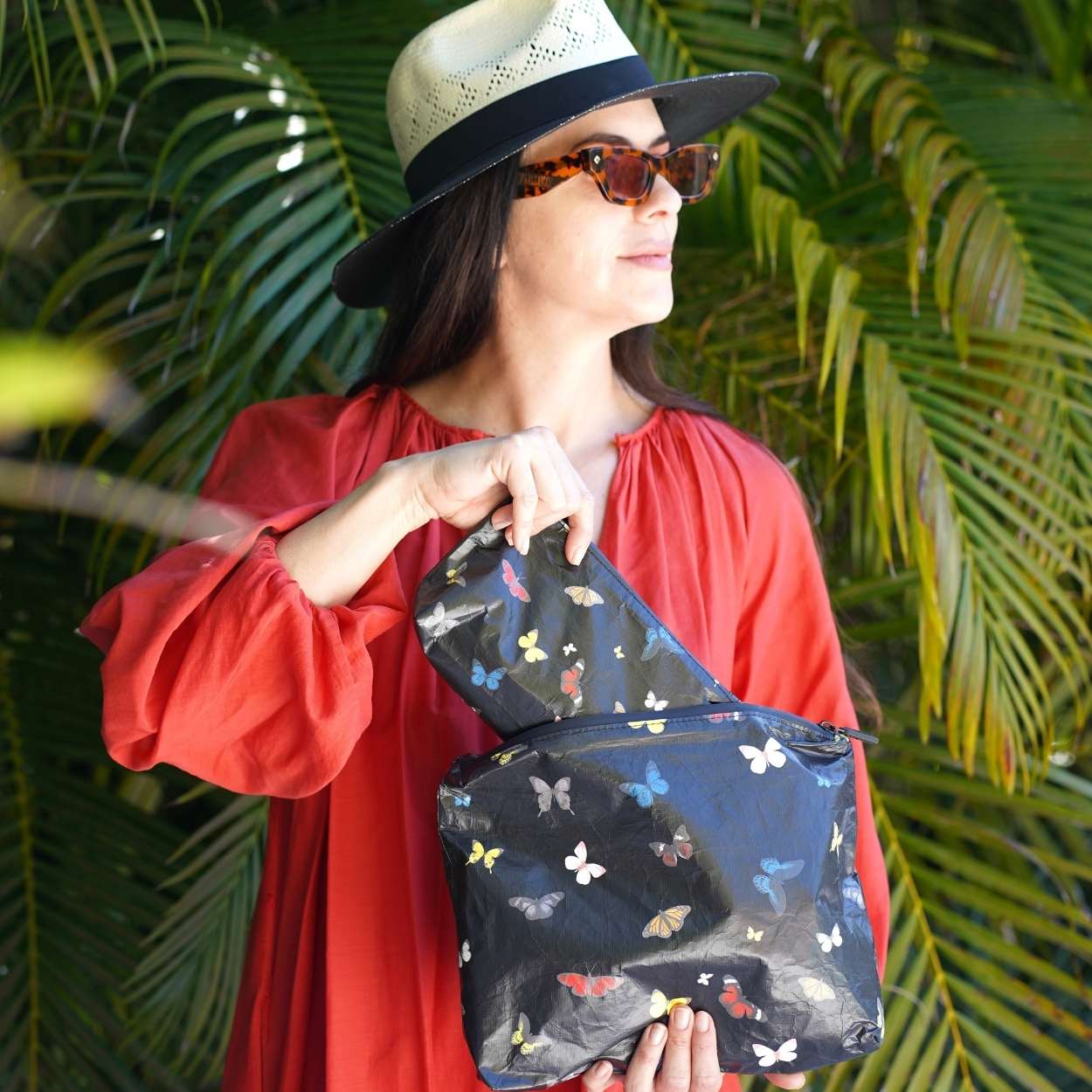 Woman holding a butterfly-patterned pouch against a green leafy background
