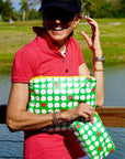 Person holding green pouches with golf balls and hearts on them outdoors by a water body