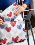 Person holding a white bag with red and blue heart patterns.