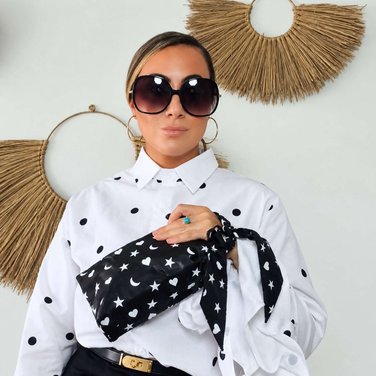 Woman wearing a matching black scarfette on her wrist with a mini zipper pouch with white hearts, moons and stars pattern.