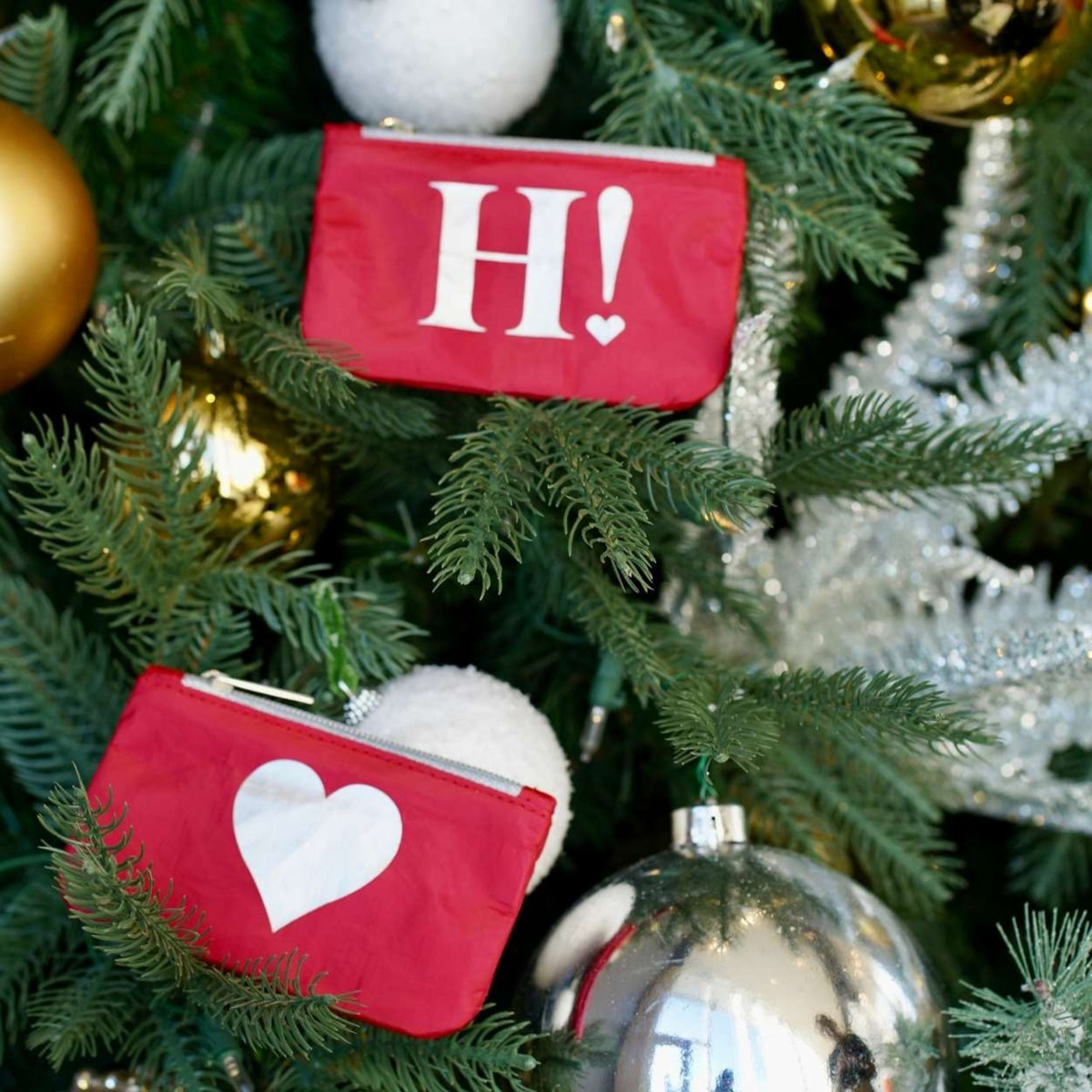 Set of two card pouches hanging on a decorated Christmas tree. The top pouch has a white 'H!' with a small heart, and the bottom pouch has a large silver heart.