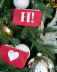 Set of two card pouches hanging on a decorated Christmas tree. The top pouch has a white 'H!' with a small heart, and the bottom pouch has a large silver heart.